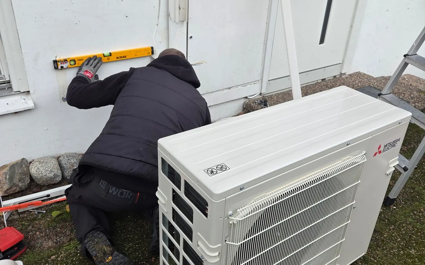 Elektriker från Bright Elteknik monterar väggfästet till en utedel från Mitsubishi Electric